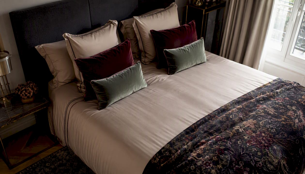 Un linge de lit raffiné, composé de plusieurs couches et rehaussé de touches de couleur profonde pour une ambiance élégante et chaleureuse.