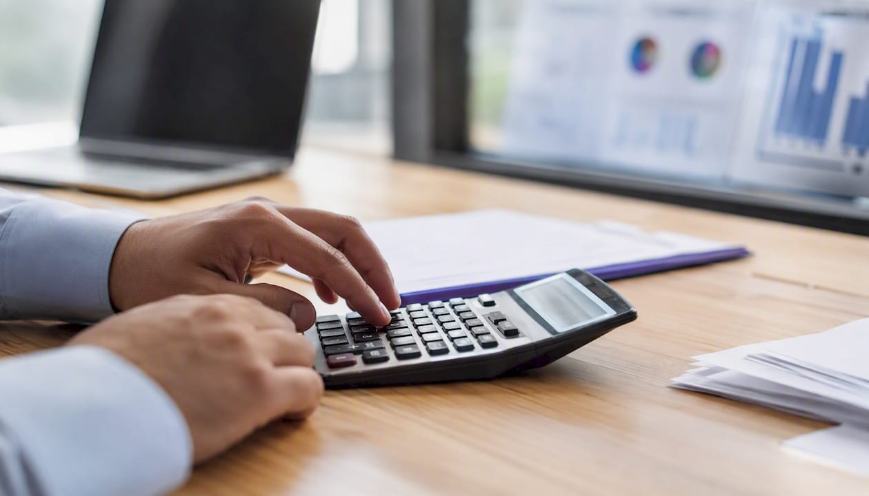 Des mains s'affairent sur une calculatrice, entourées de graphiques et de tableaux.