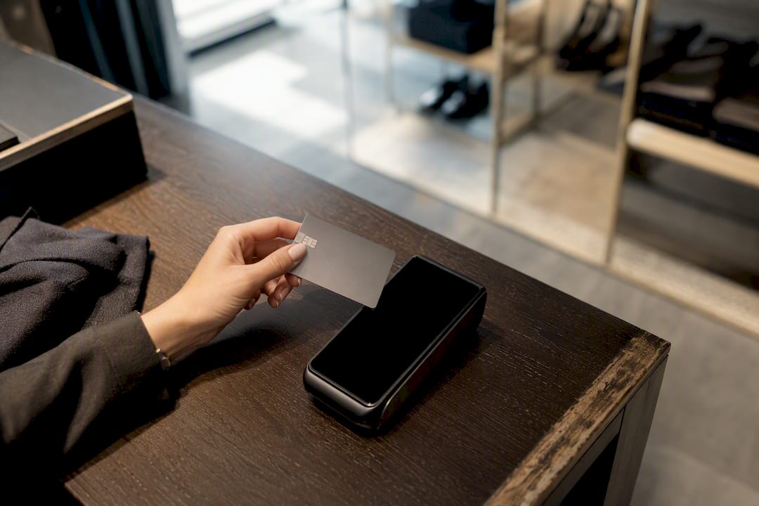 Moyens de paiement et conversion : le duo qui décide vos ventes 2 Une main présente une carte bancaire devant un terminal de paiement, entouré de symboles monétaires.