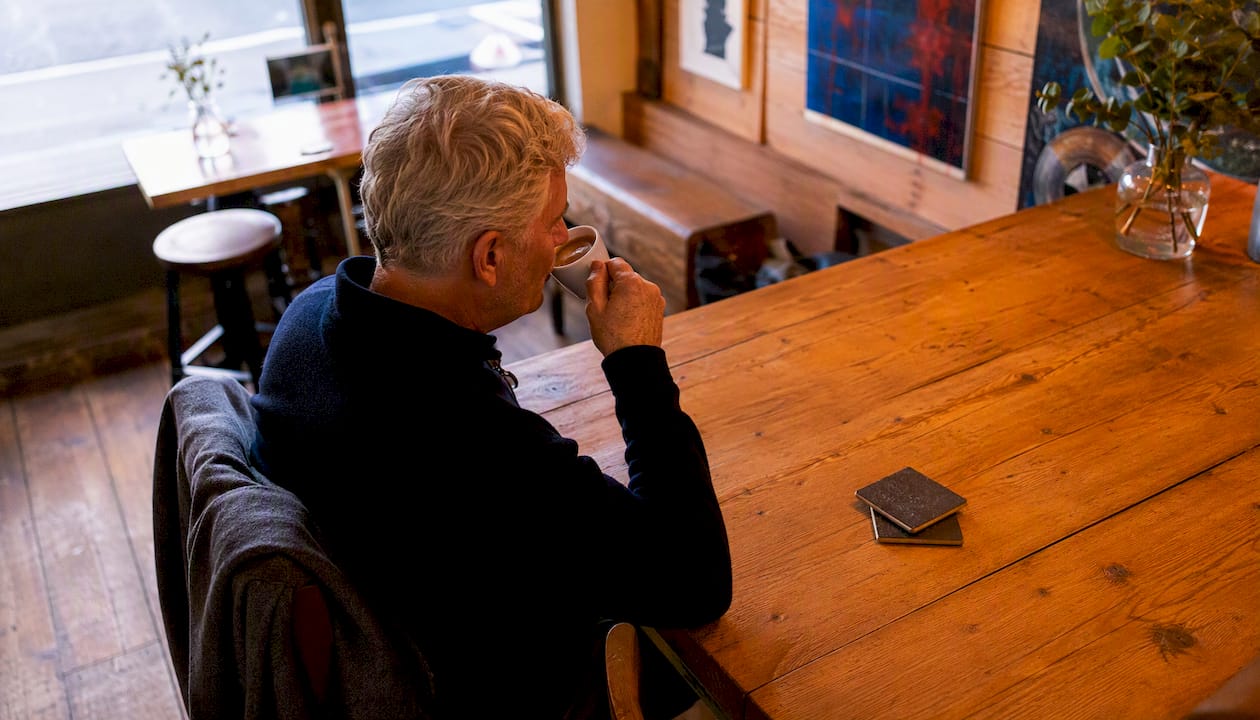 Man sitting considerately at two-person coffee shop table