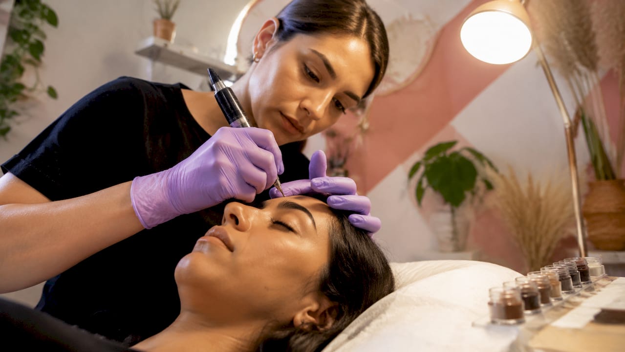 Detalle de unas manos realizando micropigmentación en las cejas con un dermógrafo