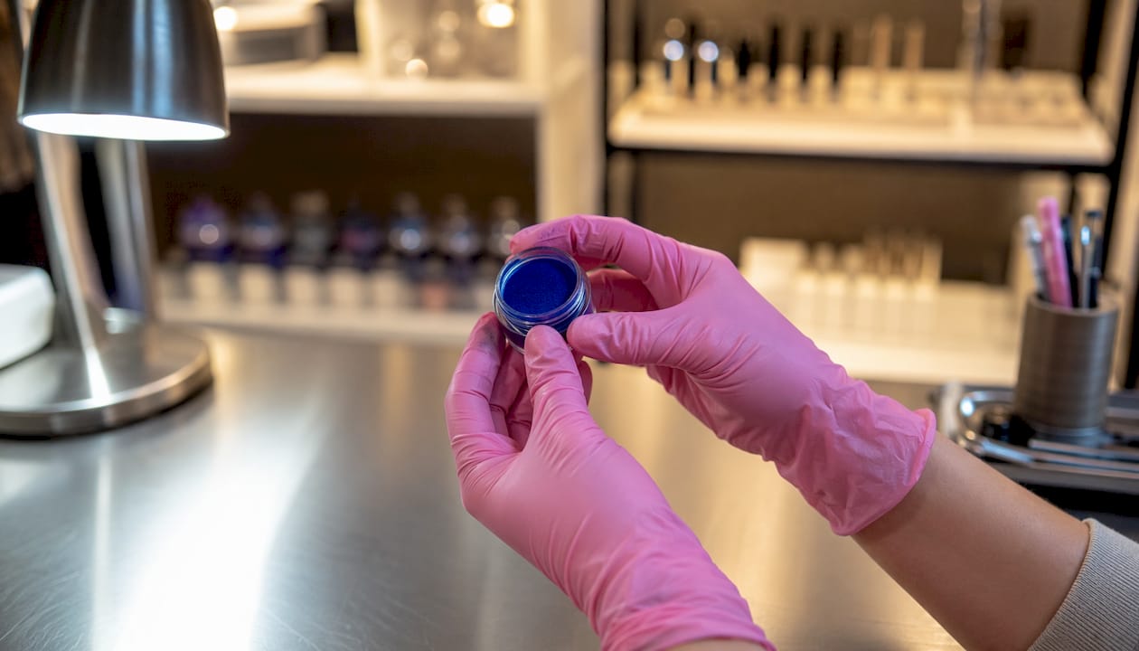 Unas manos sostienen un frasco de pigmento mineral vegano en un laboratorio de estética.