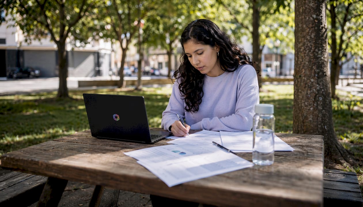Des mains tapent sur un ordinateur portable, entourées de notes de recherche sur l’intelligence artificielle, dans l’ambiance animée d’un café.
