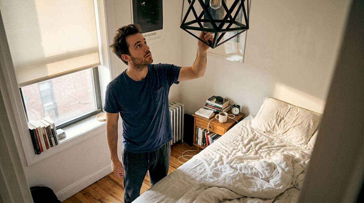 Man adjusting pendant light in bedroom