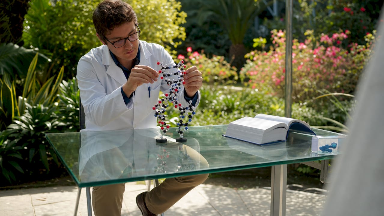 Na biurku widać dłonie, które układają model chromosomu DNA.