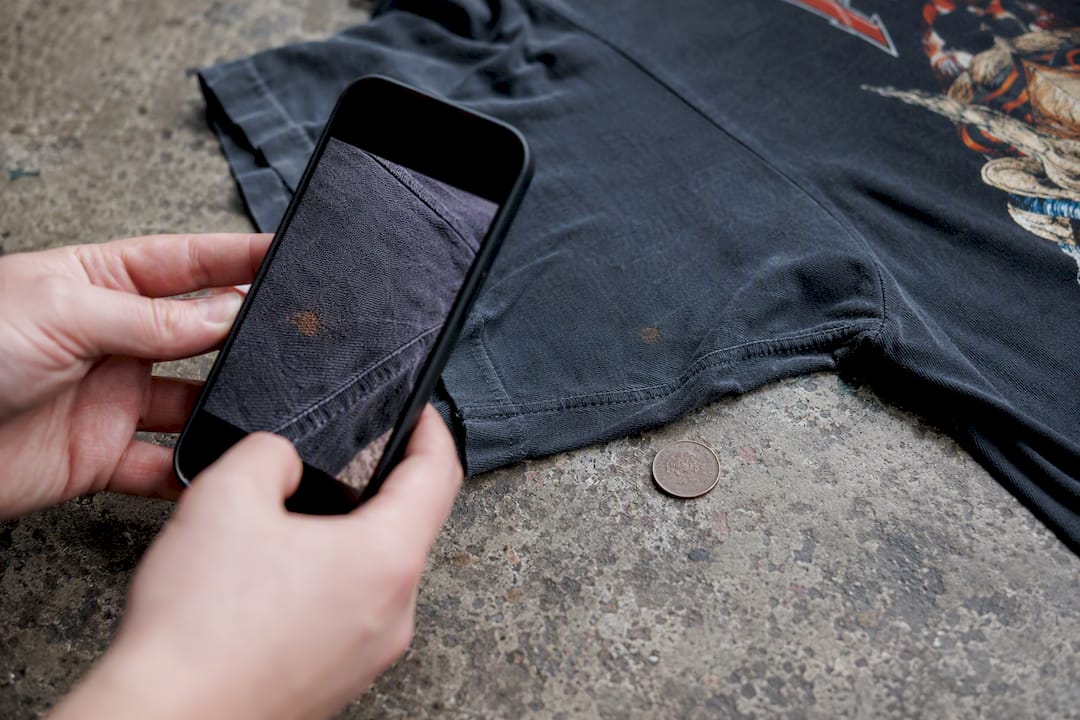 Hand photographing vintage tee flaw with coin