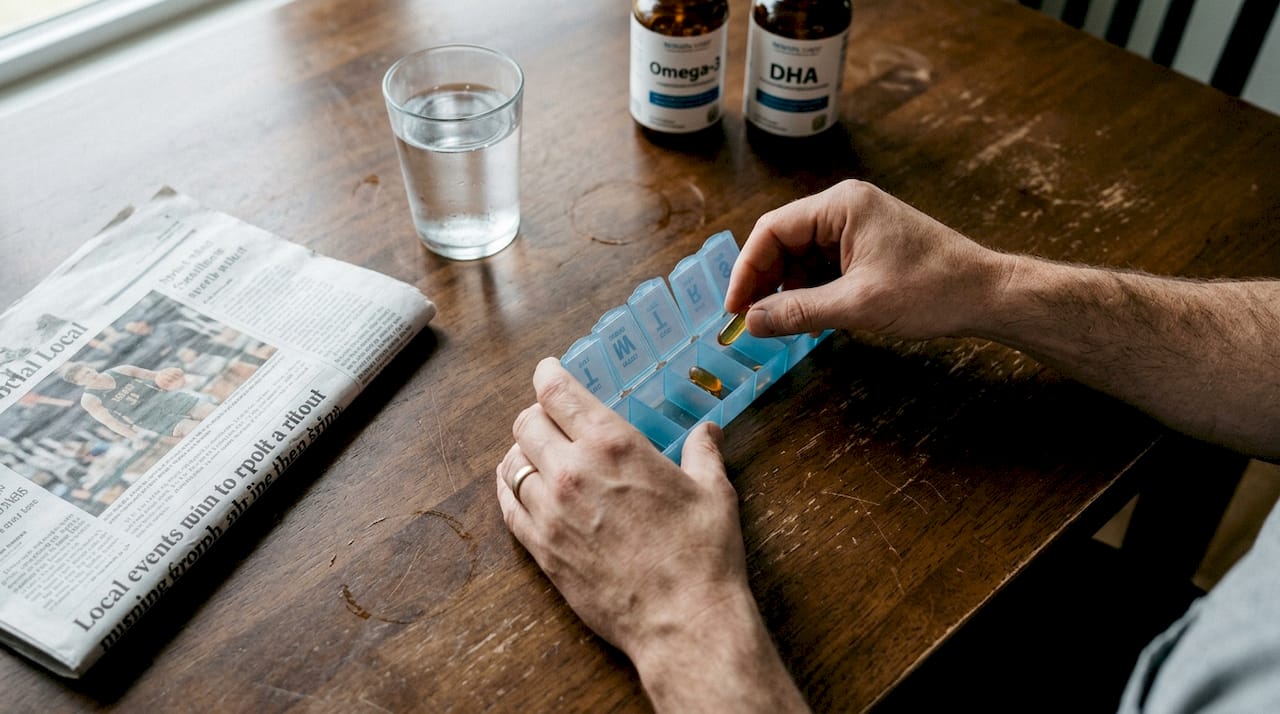 Hands opening pill organizer for omega-3 supplement