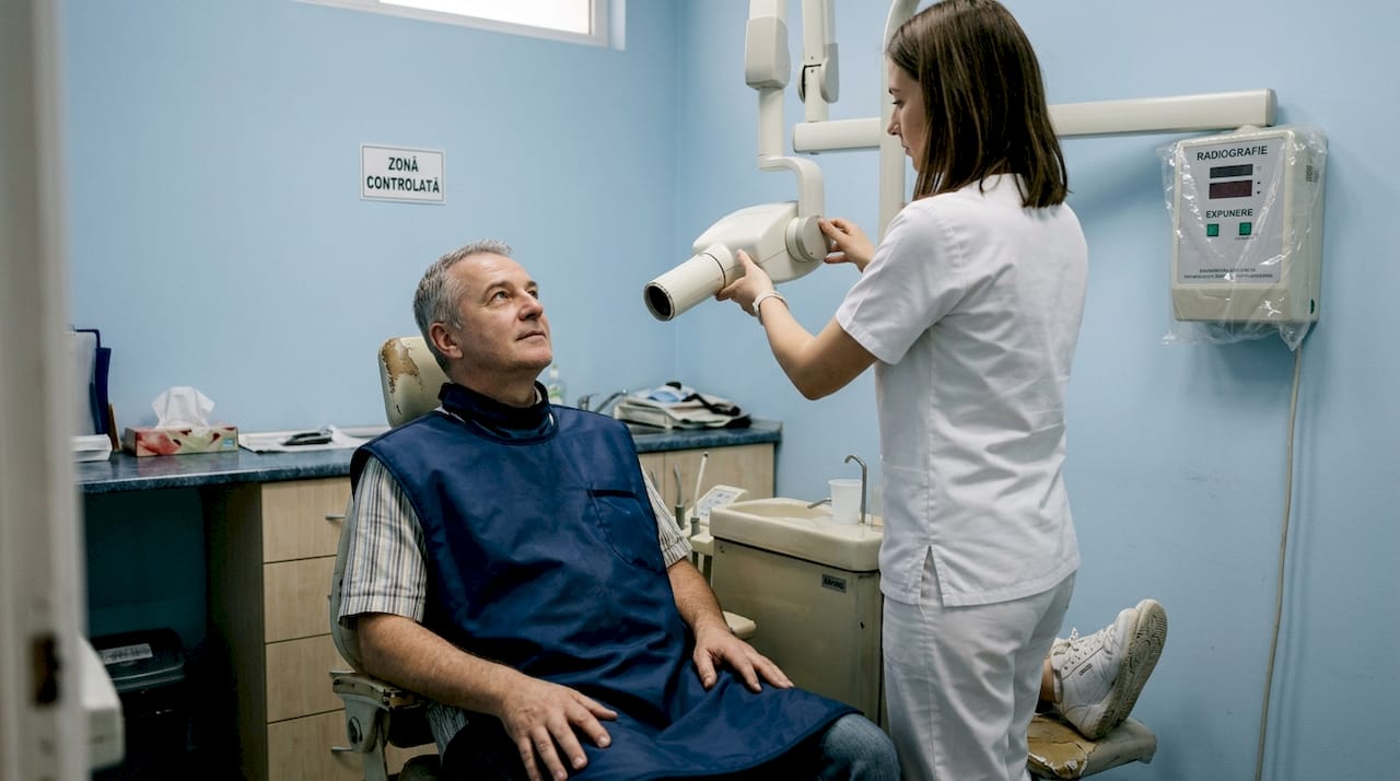 Asistentul stomatolog și pacientul în timpul efectuării unei radiografii dentare