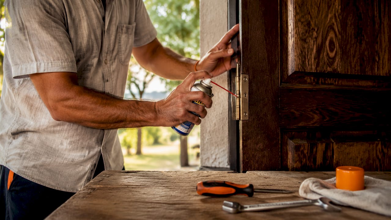 Un tecnico sta effettuando la manutenzione delle cerniere della porta d’ingresso del condominio, applicando il lubrificante per garantirne il corretto funzionamento.