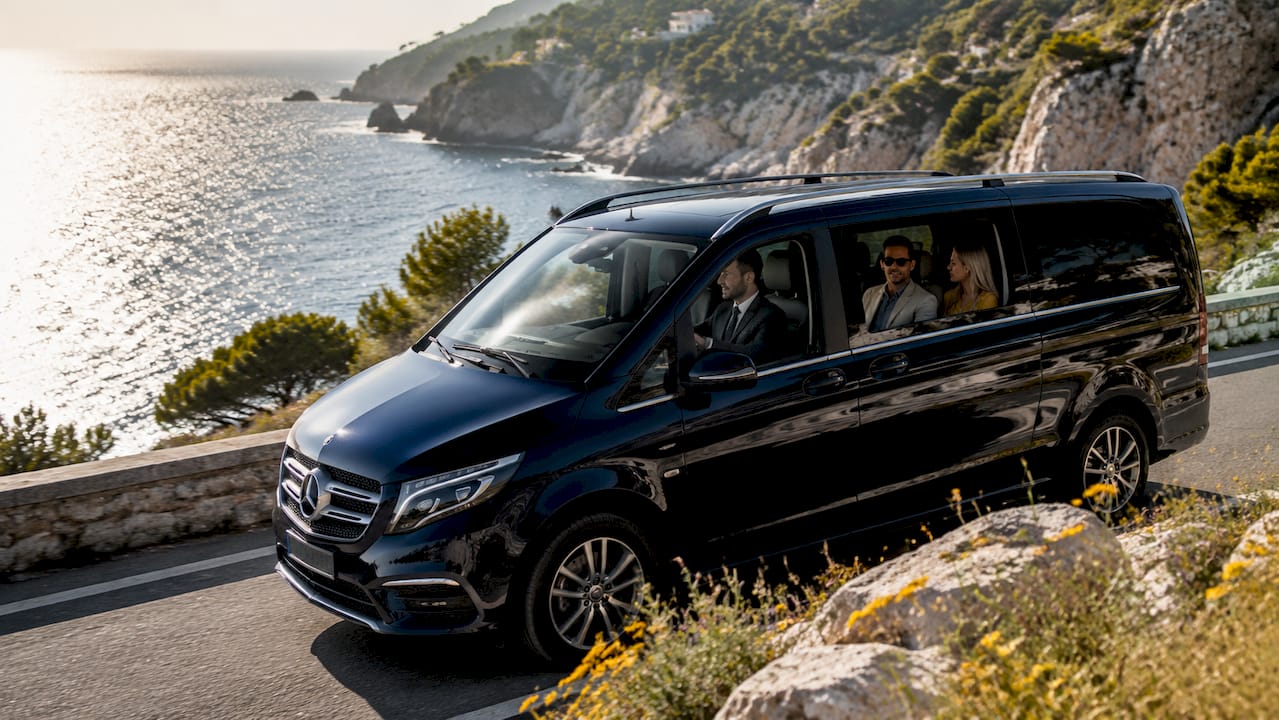 Mercedes-Benz van with chauffeur driving luxury passengers on Monaco coastal road
