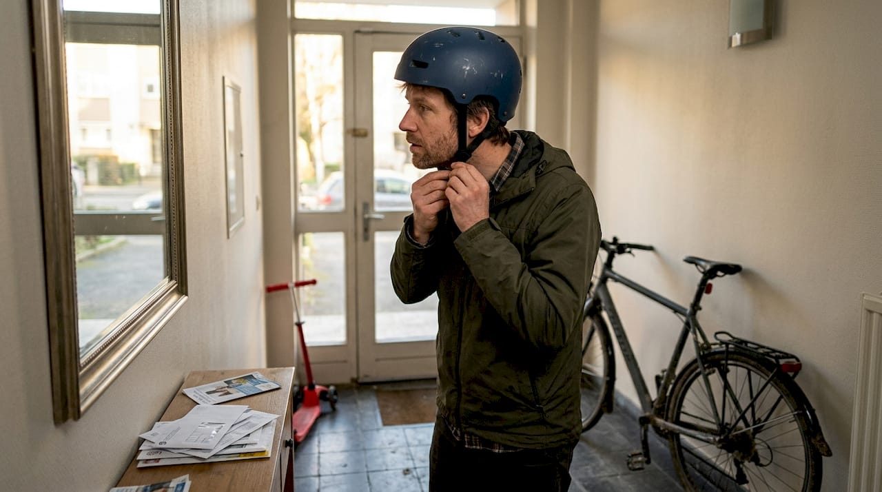 Un homme s'apprête à enfiler son casque de vélo devant un bâtiment.