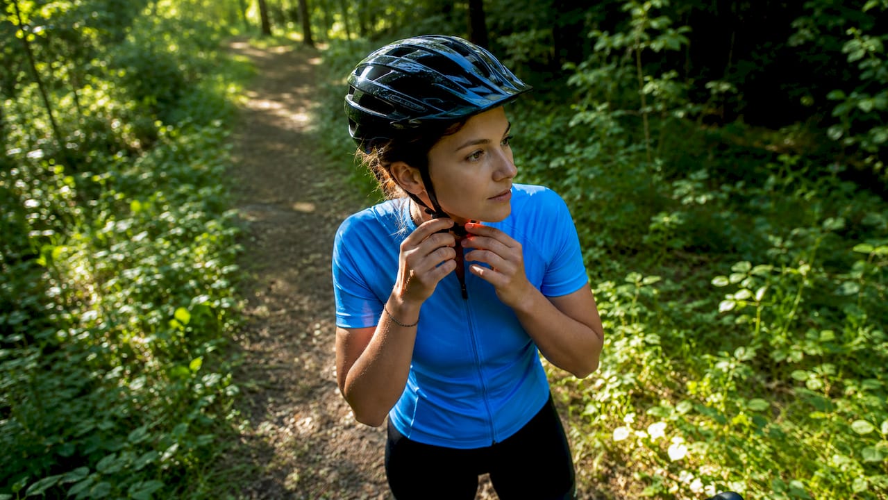 Une femme ajuste son casque de vélo sous le soleil, au cœur d’un parc.