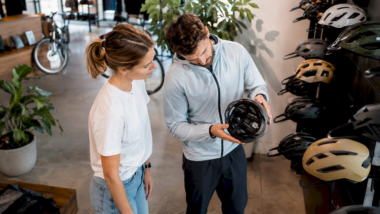 Des clients examinent les casques de vélo en boutique, vérifiant leur qualité et leur ajustement.