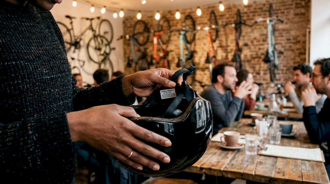 Des mains tiennent un casque sur lequel est apposée une étiquette d’homologation.