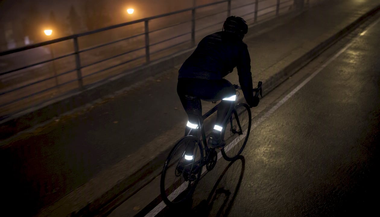 Au crépuscule, on aperçoit les jambes du cycliste, entourées de bandes réfléchissantes, qui s’activent à chaque coup de pédale.