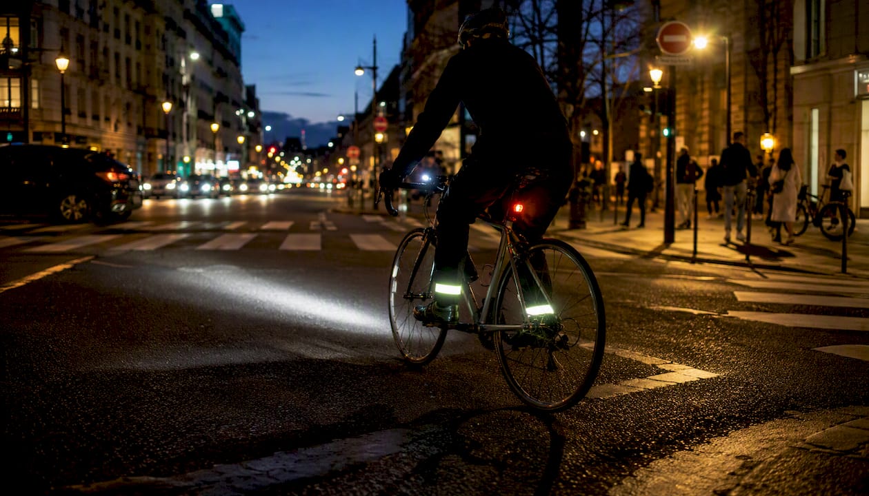 Un cycliste circule de nuit en ville, éclairé par les lumières de son vélo.