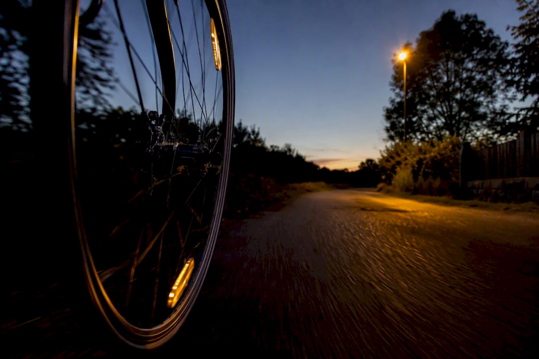 À la tombée de la nuit, la roue du vélo tourne rapidement, ses rayons réfléchissants créant des éclats de lumière dans la pénombre.
