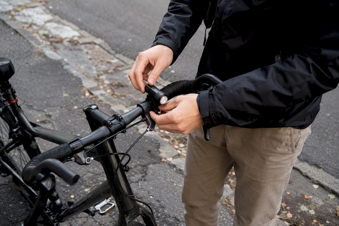Sur un trottoir abîmé en ville, une main ajuste le phare du vélo pour continuer à pédaler en toute sécurité.
