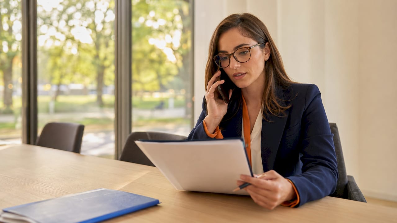 Agente assicurativa al telefono mentre consulta documenti relativi a proprietà immobiliari