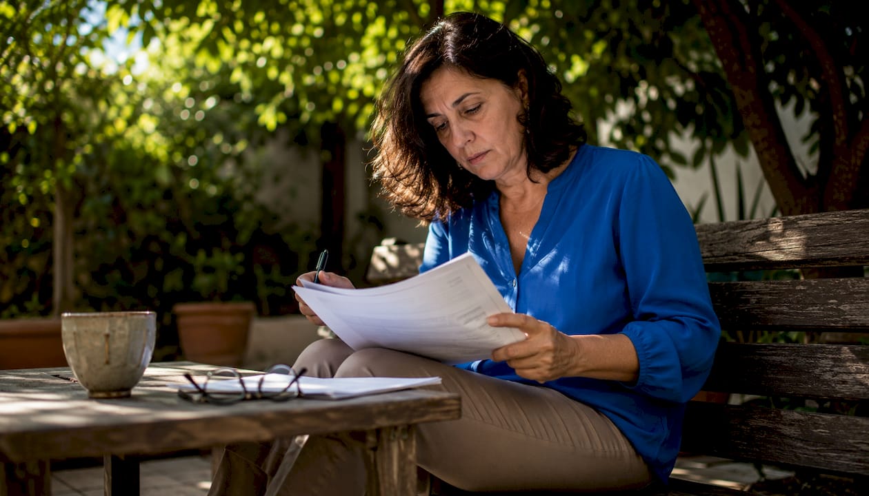 Donna che controlla attentamente delle carte relative all'acquisto di una casa, seduta al tavolo del soggiorno.