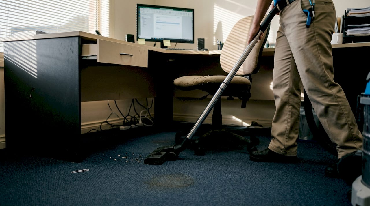 Janitor vacuuming carpet under office desk