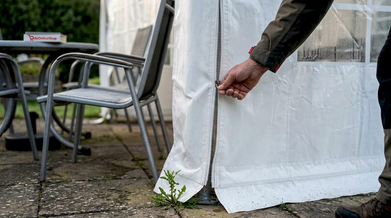 Iemand ritst de zijwand van de partytent dicht met zijn hand.