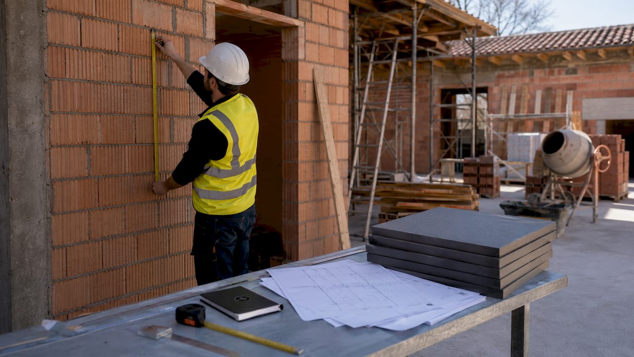 Der Bauleiter nimmt direkt auf der Baustelle Maß am Mauerwerk.