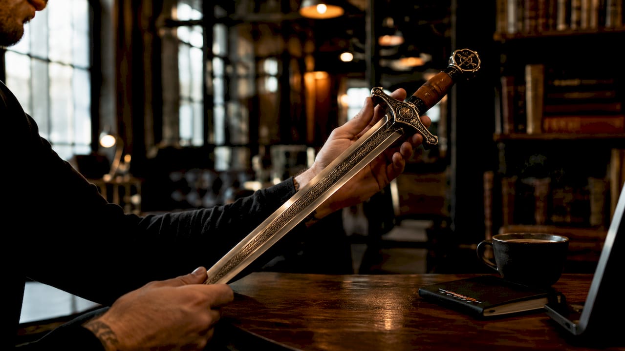 Hands holding ornate symbolic sword over wooden table