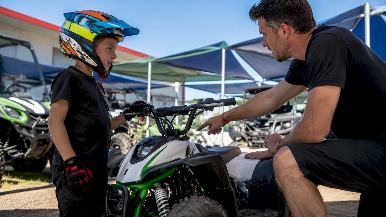 Child wearing helmet beside youth ATV indoors