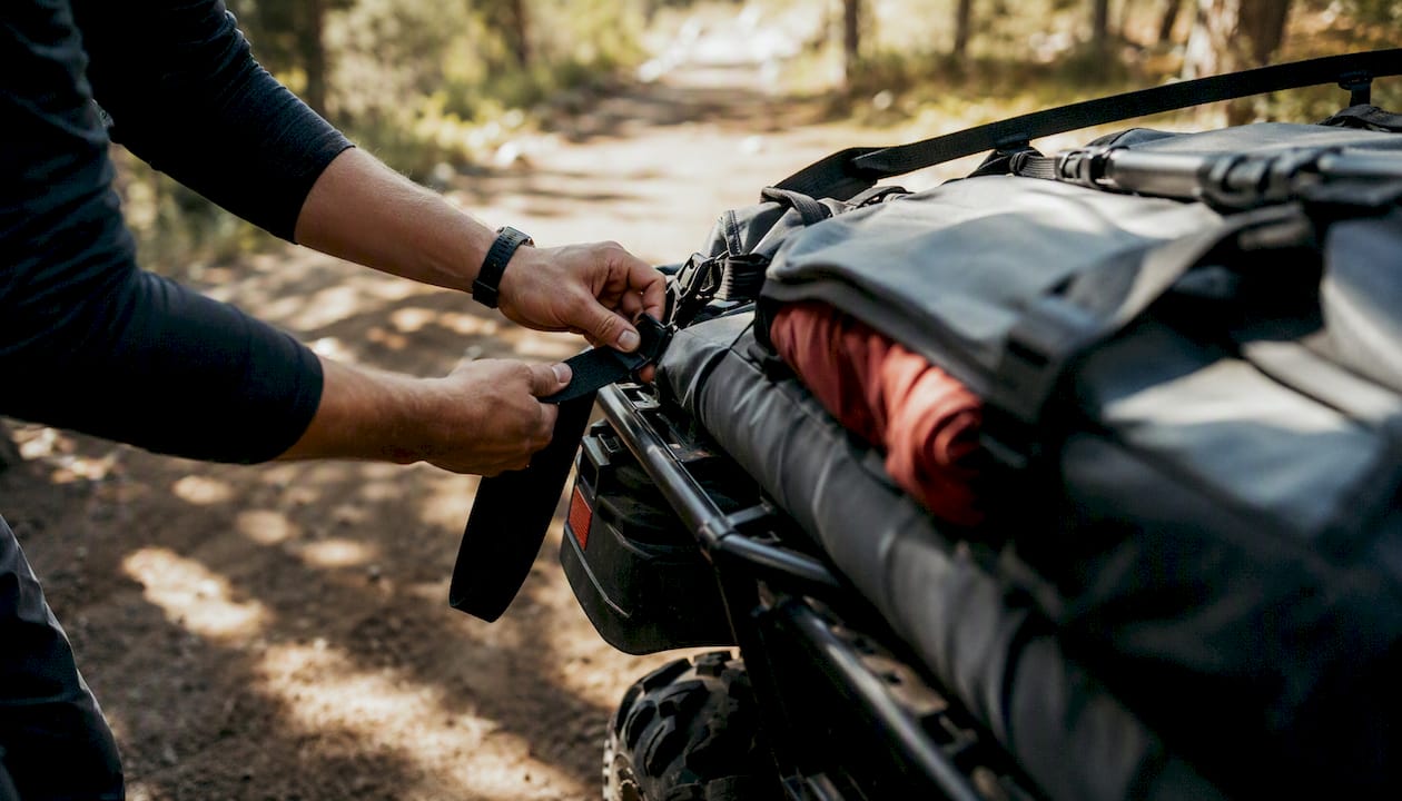 Hands securing gear on ATV rack