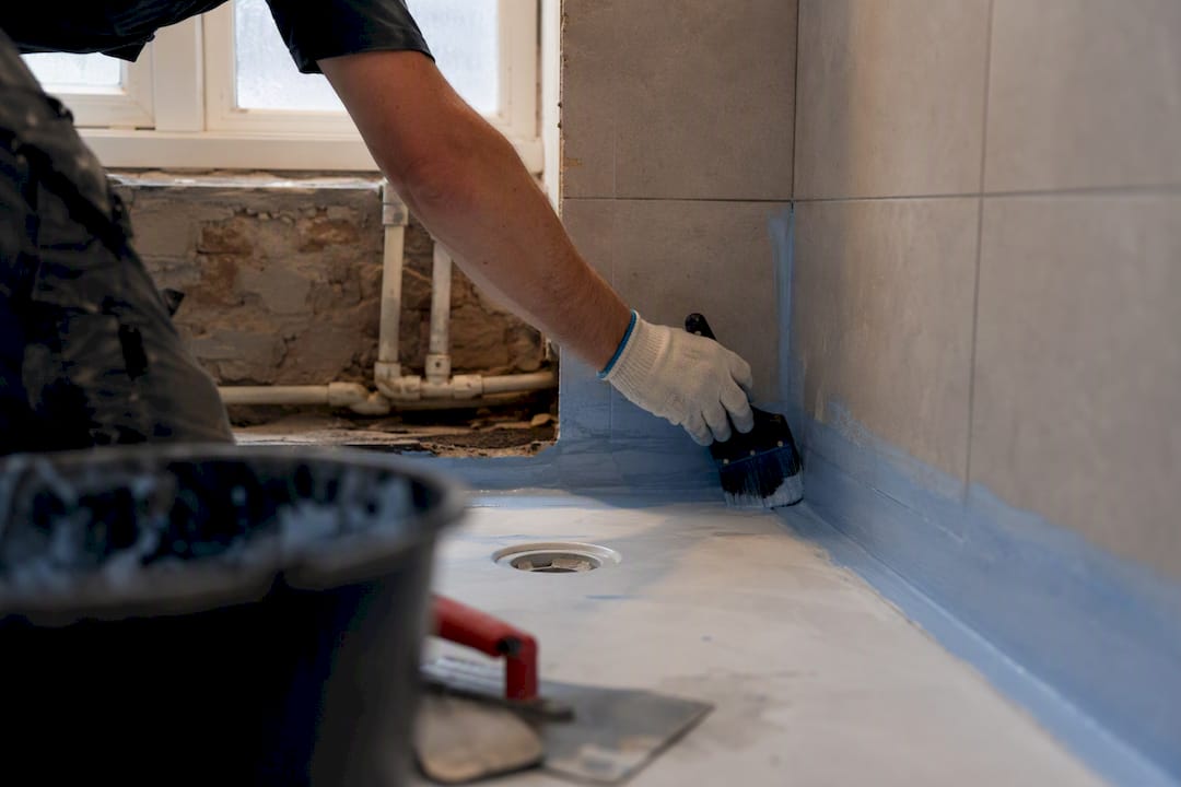 Hands applying waterproofing membrane in shower area