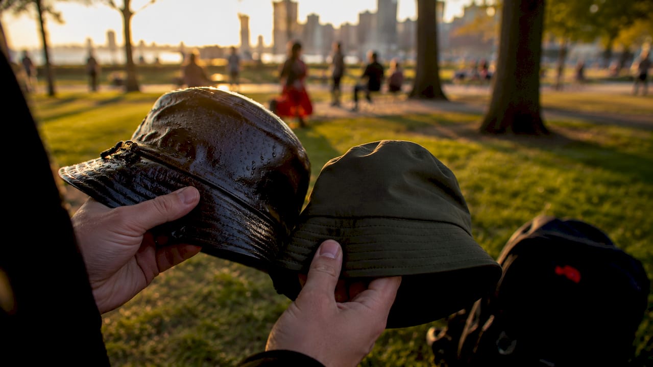 Hands comparing oilskin and technical fabric hats outdoors
