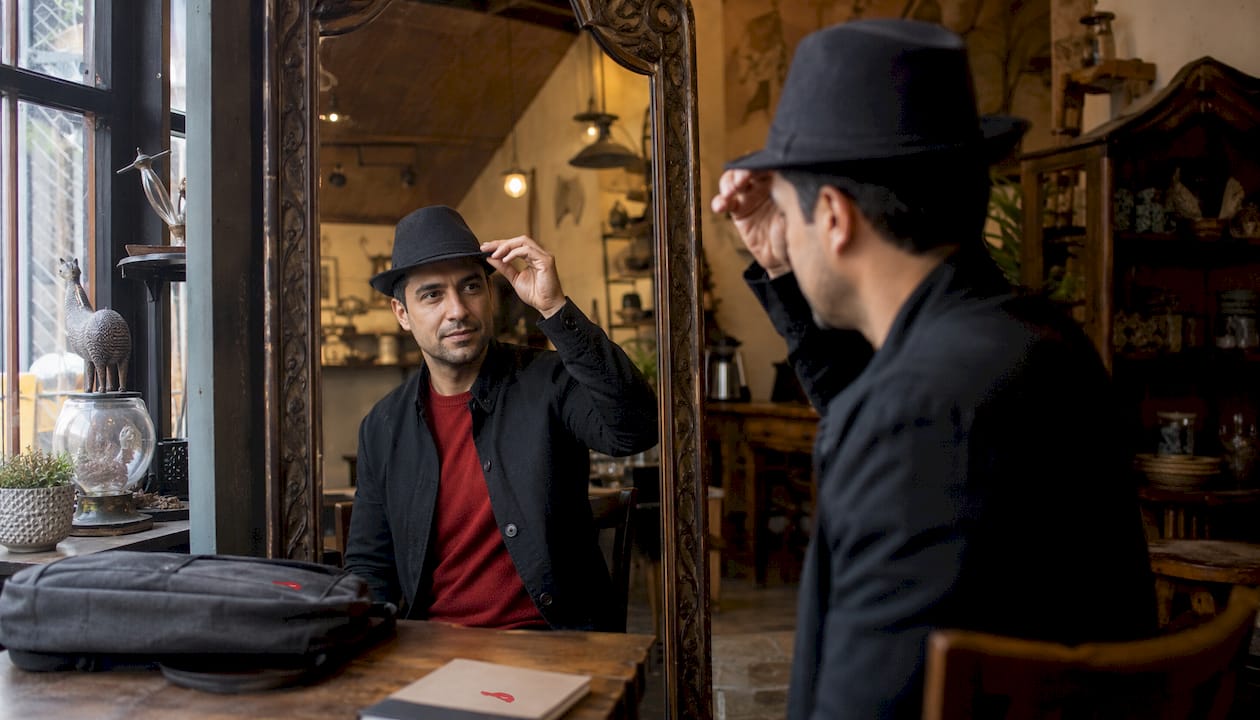 Man adjusting fedora in mirror