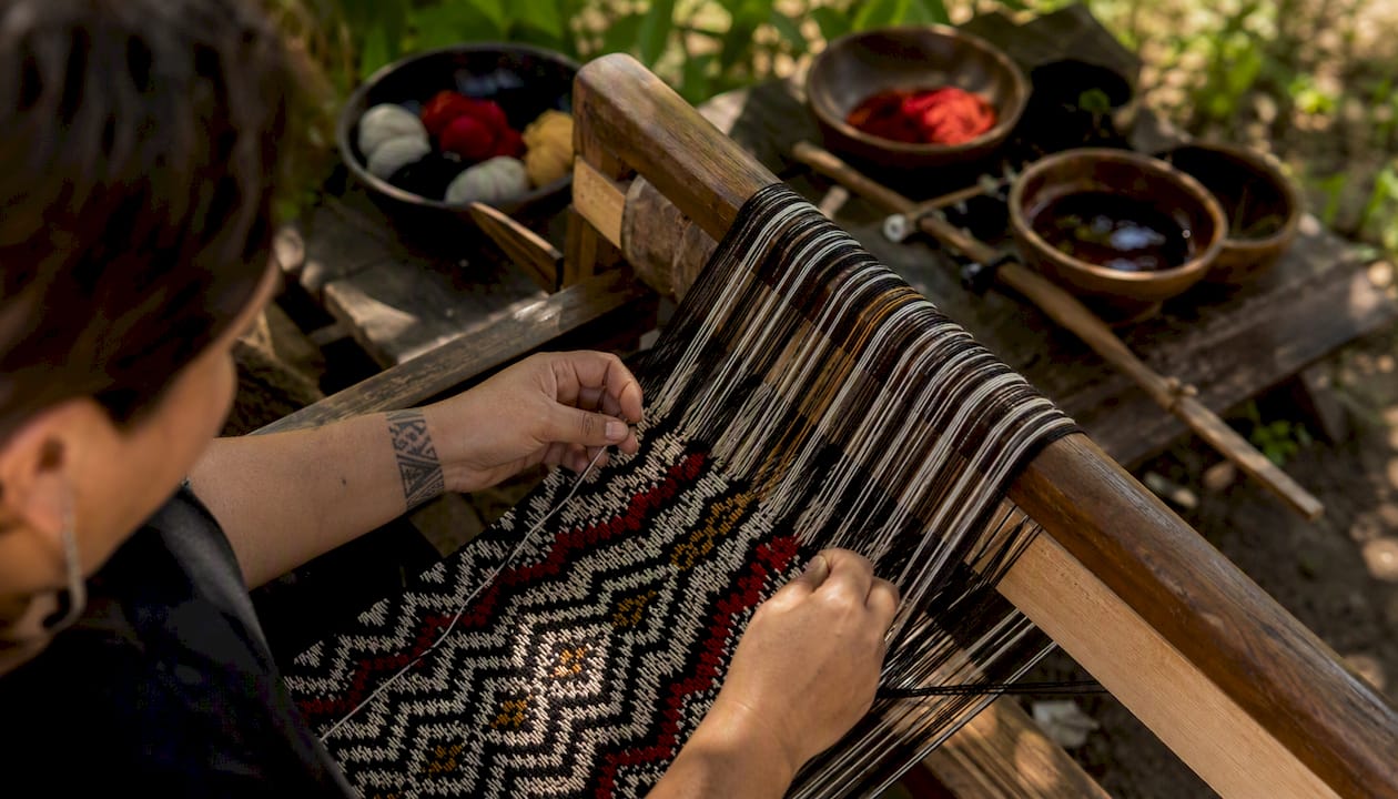 Hands weaving tāniko pattern on loom