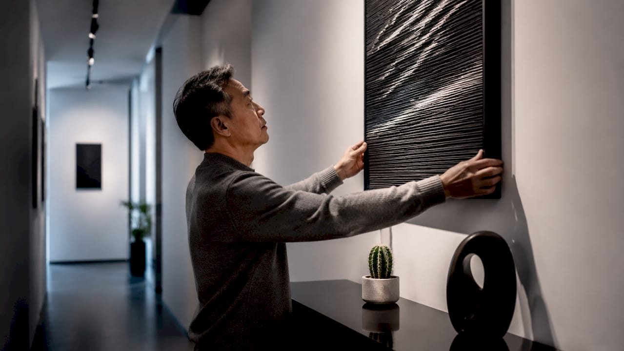 Man hanging art in narrow hallway
