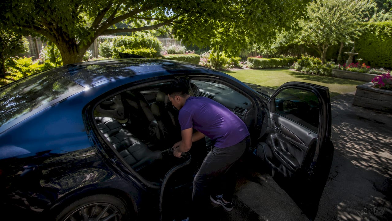 Hands vacuuming car seat upholstery