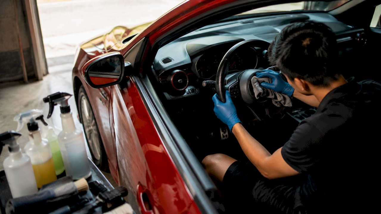Hands wiping car dashboard interior during detailing