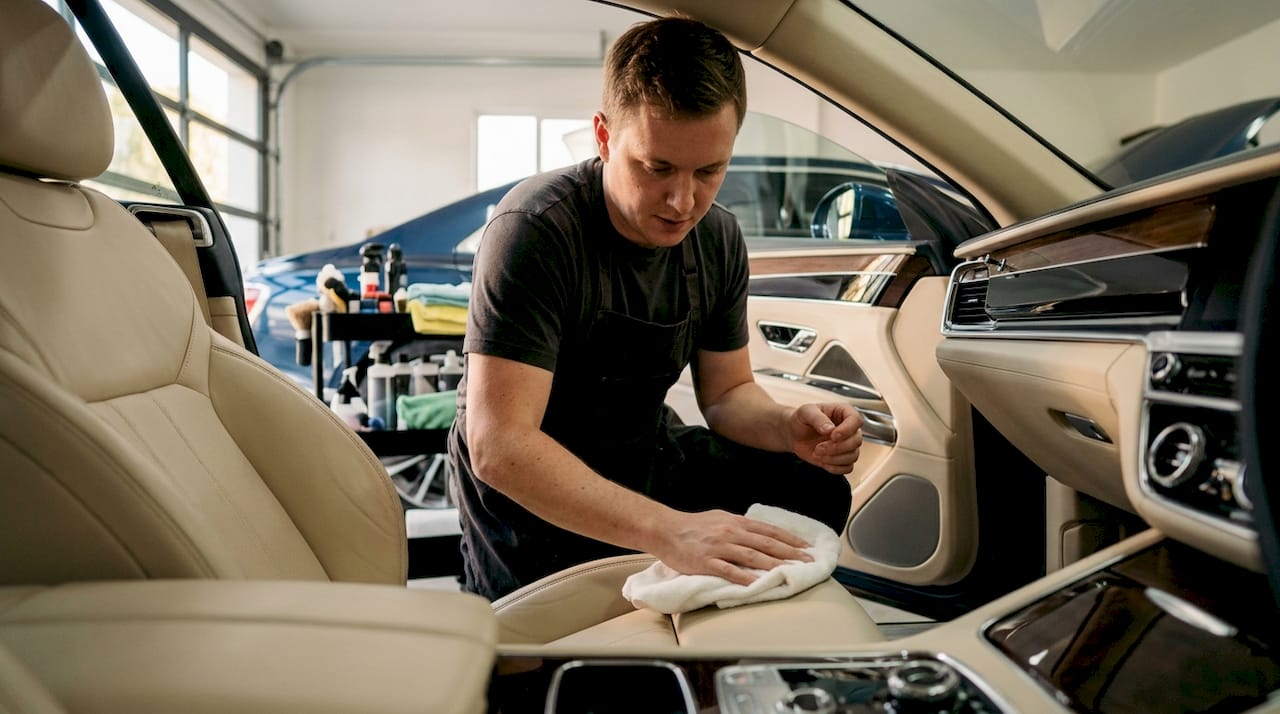 Hands applying conditioner on black leather car seat