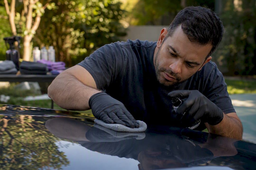 Hands removing adhesive residue on coated vehicle panel