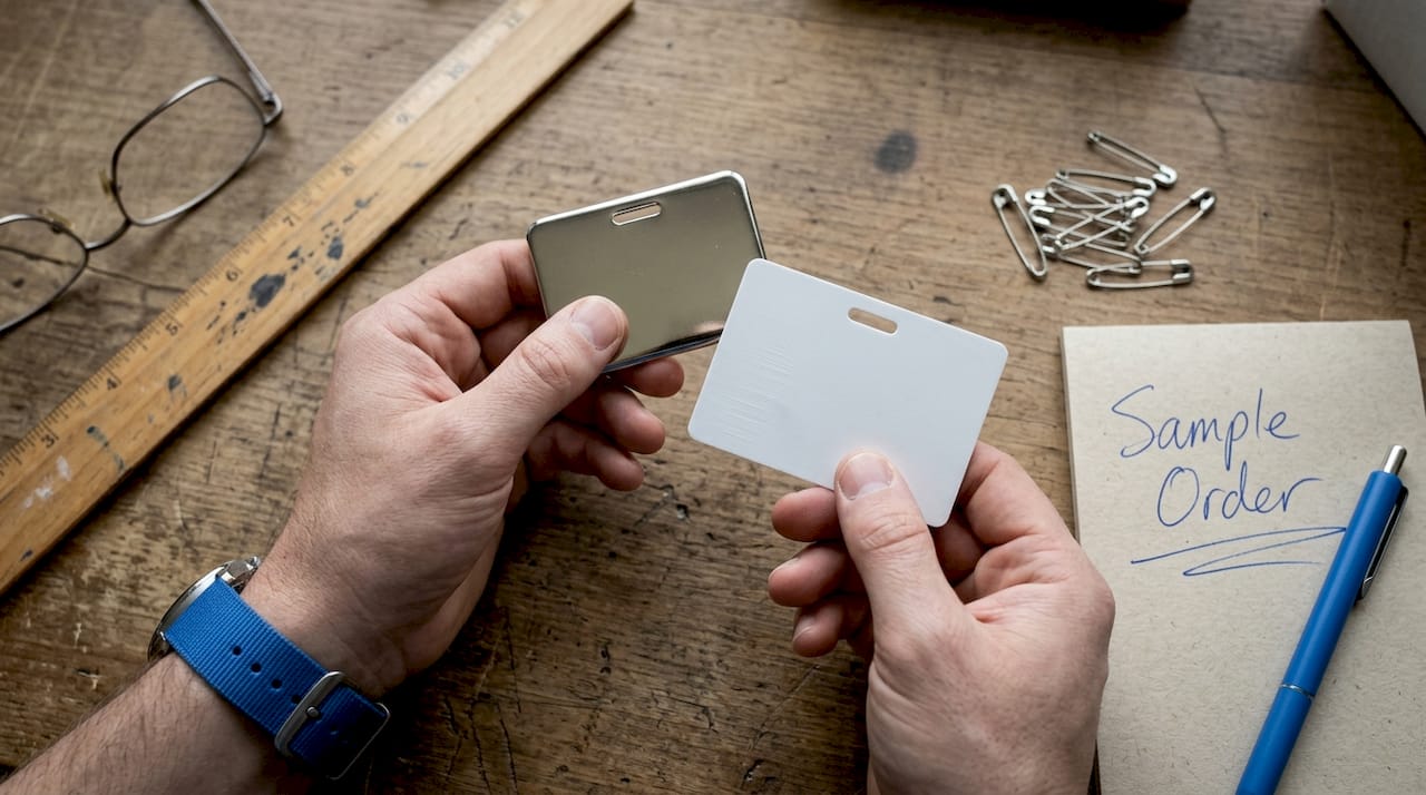 Hands comparing metal and plastic badge blanks