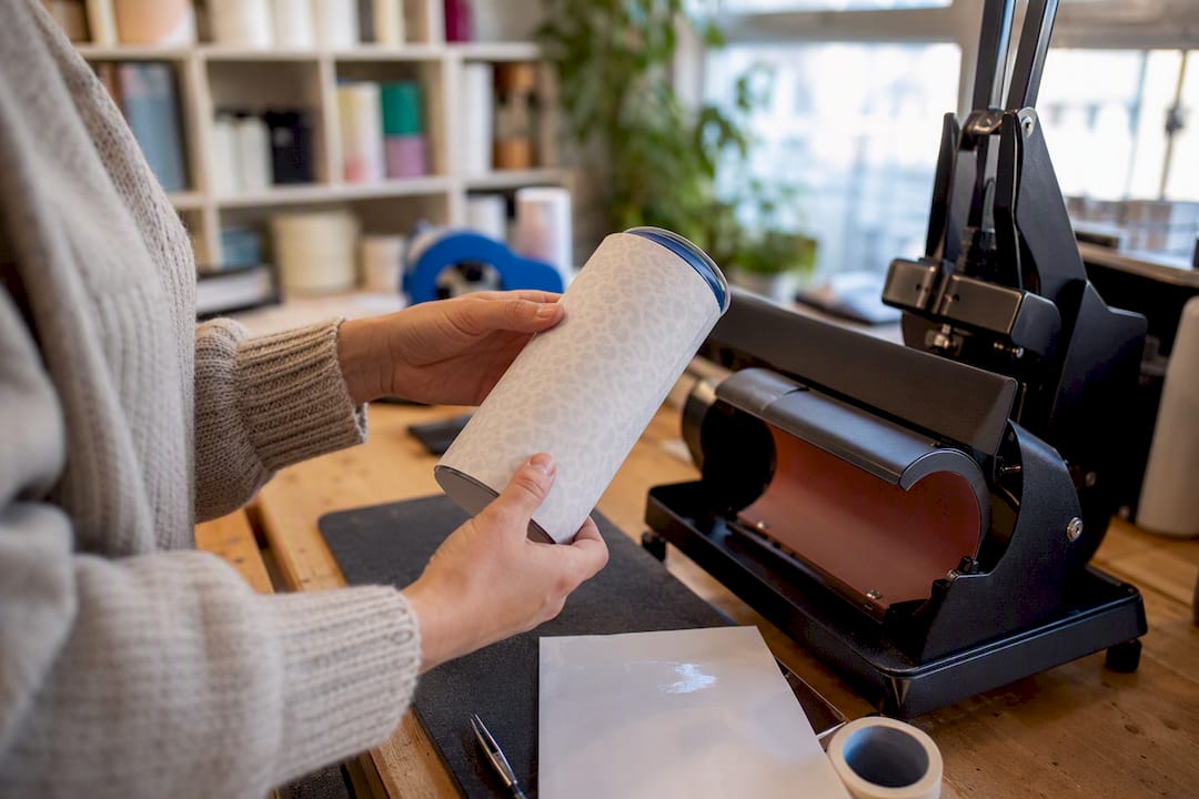 Hands aligning sublimation transfer on coated tumbler