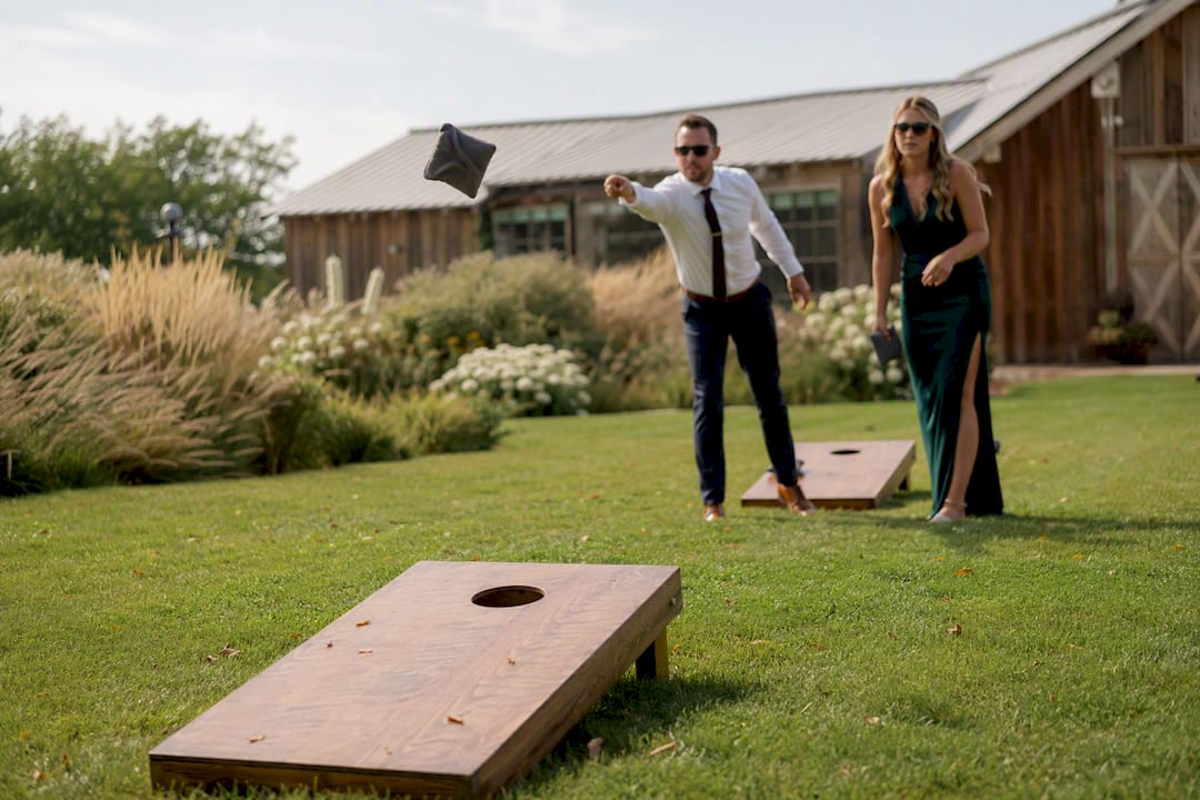 Couple playing cornhole at outdoor wedding