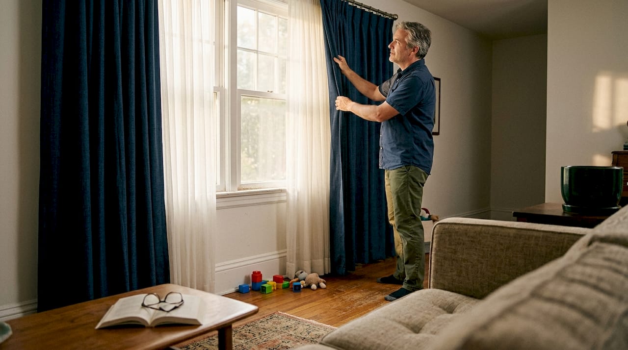 Person adjusting lined curtains to prevent sun fading