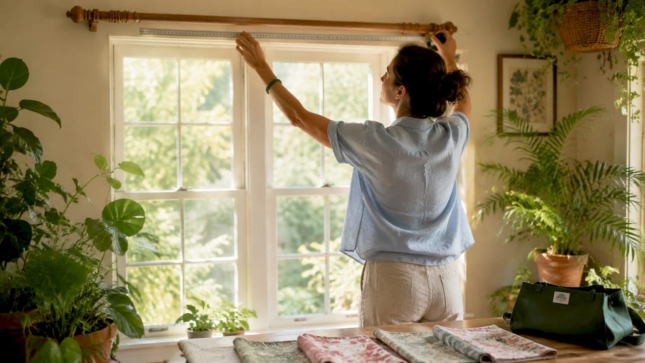 Hands measuring curtain rod width closely