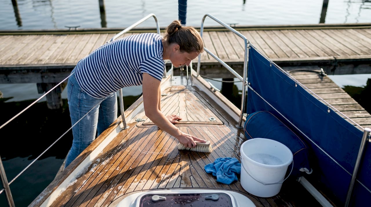 Een vrouw maakt het dek van een luxe sloep schoon.