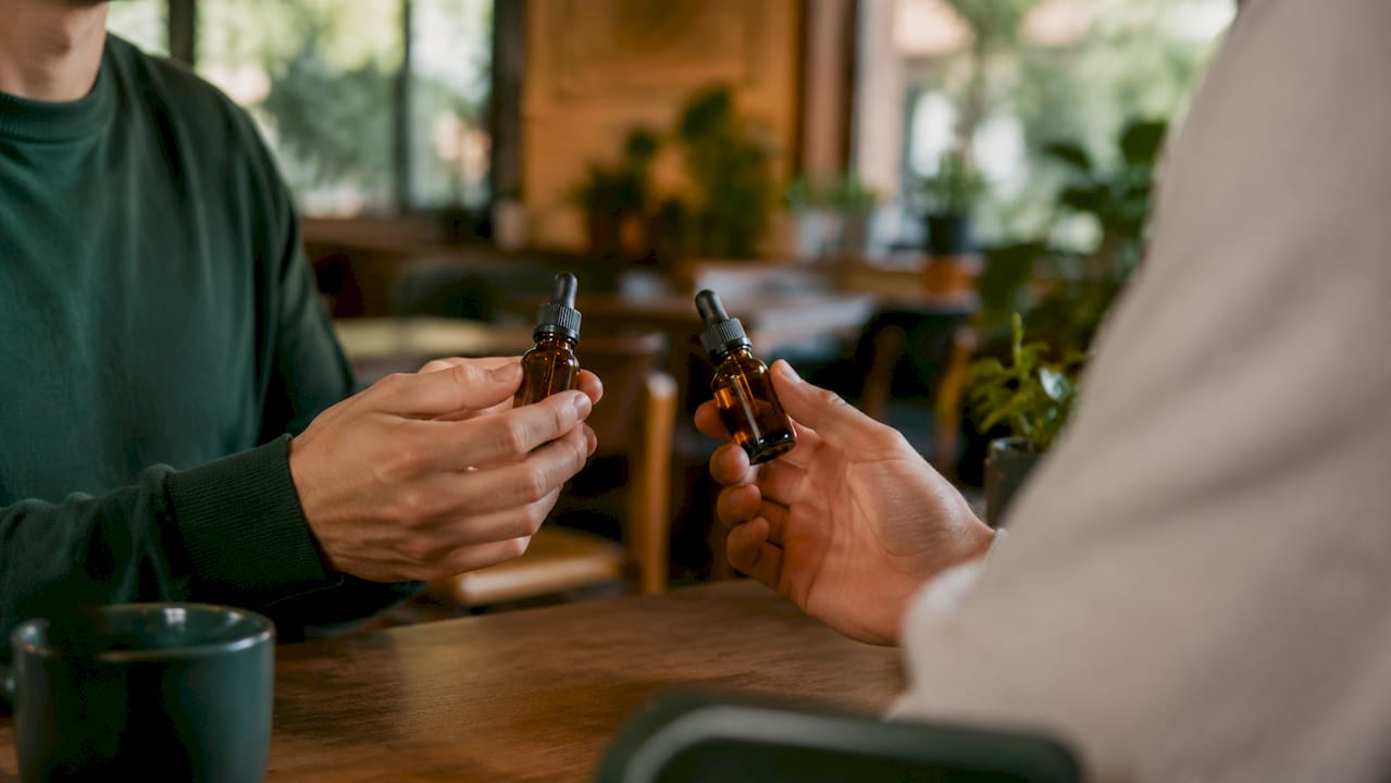 Händer som håller flaskor med CBD- och THC-olja