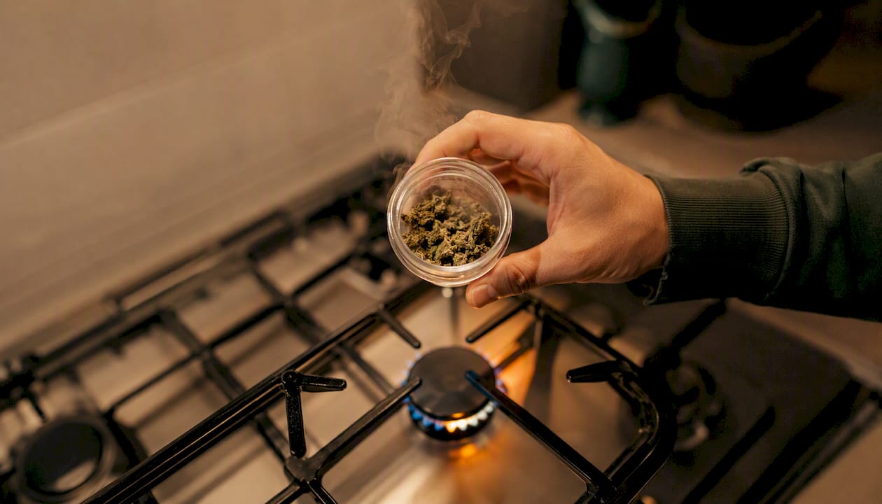 Värmer cannabis i ett glasbehållare på spisen med handen.