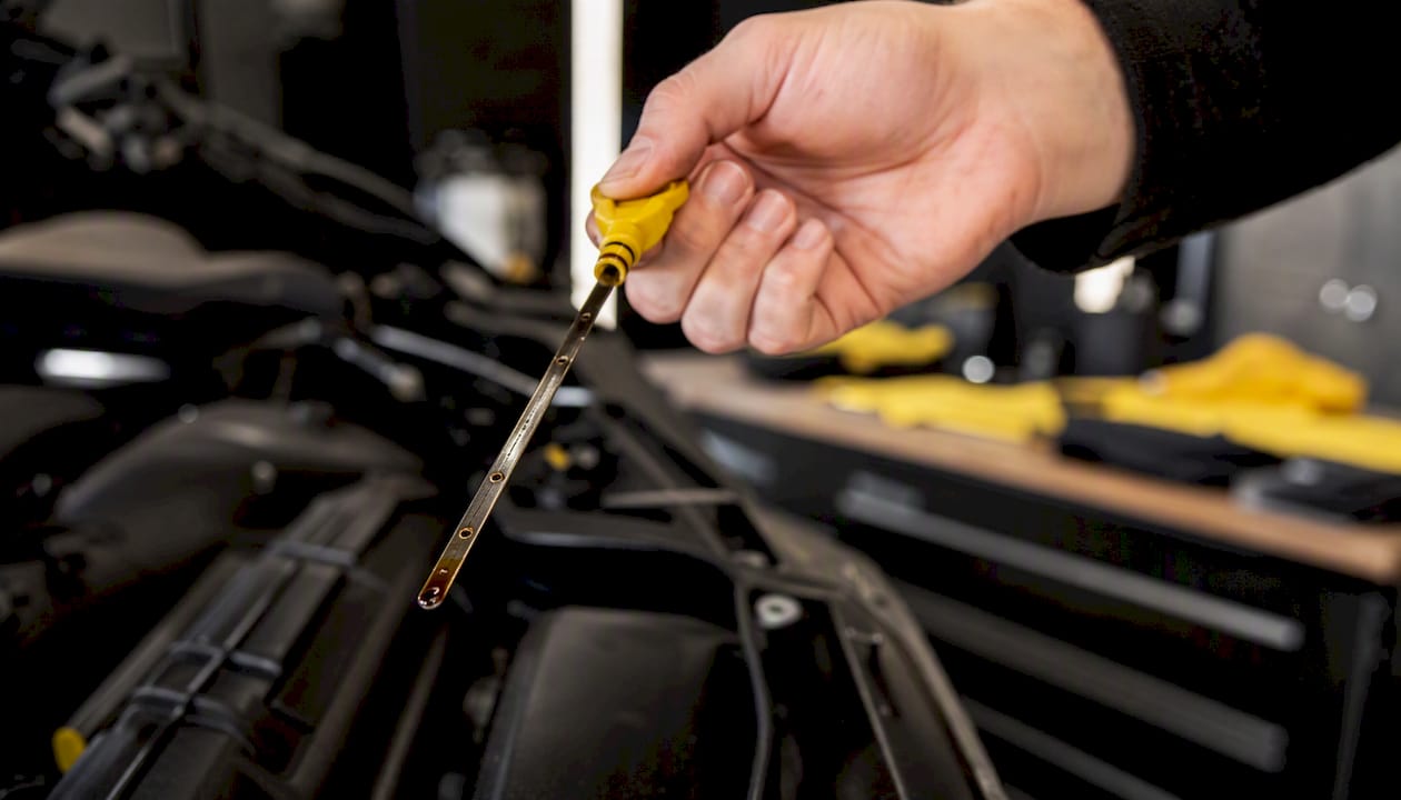Hand pulling engine oil dipstick in garage