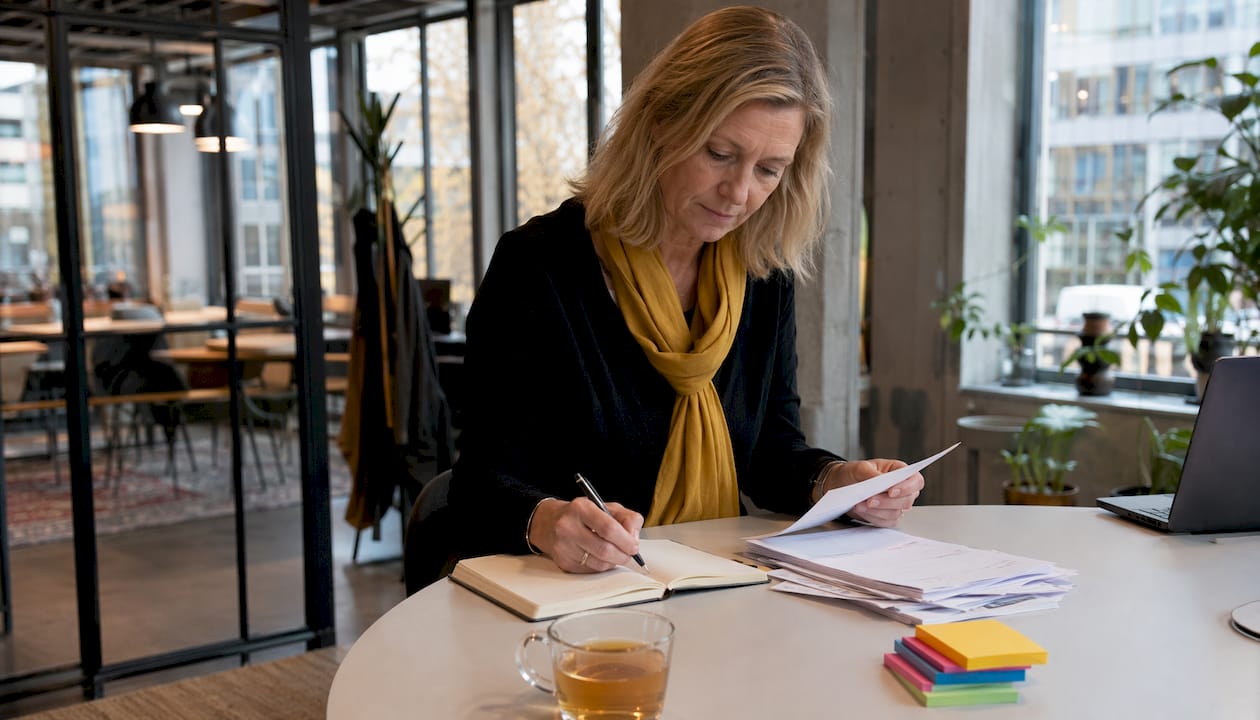 En kvinna sitter vid sitt skrivbord och går igenom sina fakturor.