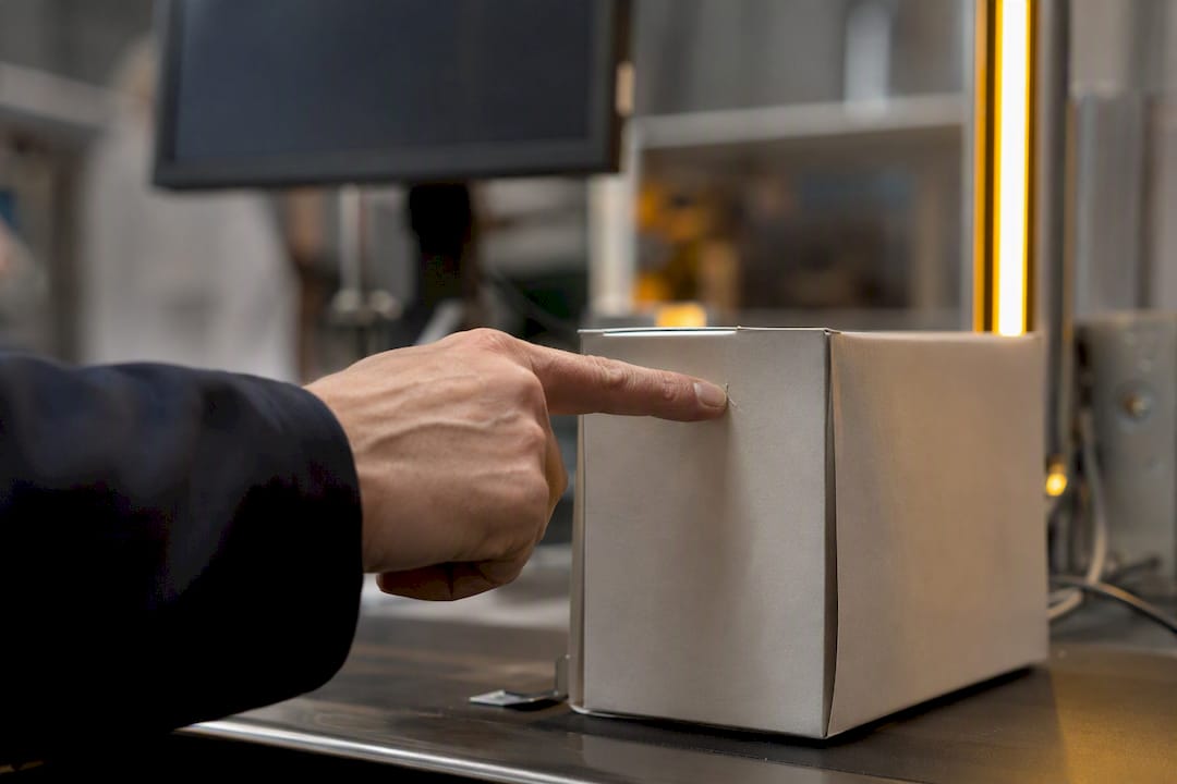 En hand pekar på en detalj på produktens förpackning.